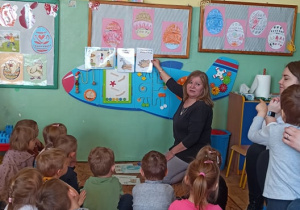 Nauczycielka pokazuje ilustracje przedstawiające czynności higieniczne zawieszone na tablicy.
