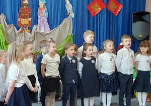 Dzieci w strojach galowych śpiewają piosenkę o Polsce.