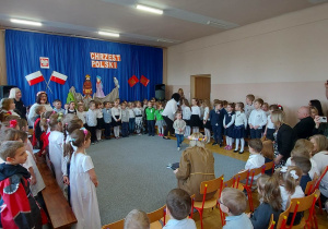 Dzieci w strojach galowych śpiewają piosenkę o naszym kraju.