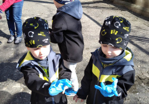Dzieci zakładają rękawiczki ochronne. Przygotowują się do zbierania śmieci.