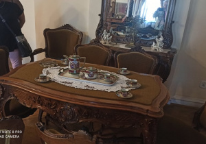 Na środku stoi starodawny stół. Na stole leży mała serwetka. Na serwetce stoi serwis kawowy.
