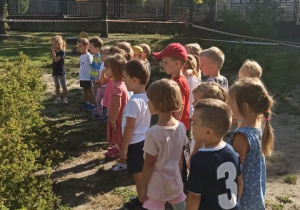 Dzieci stoją w szeregu w ogrodzie przedszkolnym. Patrzą przed siebie.