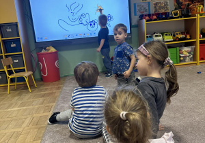 Dzieci przyglądają się jak rysuje na monitorze interaktywnym inne dziecko.