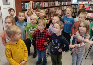 Dzieci stoją w bibliotece. Uśmiechają się.