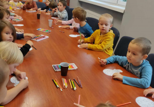 Dzieci siedzą przy stole. Kolorują kolorowankę baloniki.