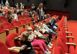 Dzieci siedzą w czerwonych fotelach w teatrze.