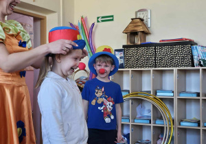 Dzieci biorą udział w pokazie cyrkowym na scenie z kapeluszami na głowie.