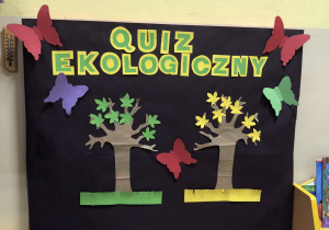 Tablica z napisem quiz ekologiczny. Na tablicy przypięte dwa drzewa. Jedno ma zielone listki, drugie żółte listki.