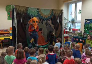 Dzieci oglądają przedstawienie. Na scenie pojawiła się osoba przebrana za lisa. Za nim dekoracja las.