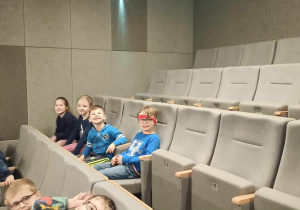 Dzieci siedzą w kinie na fotelach.
