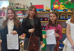 Cztery dziewczynki ze Szkoły Muzycznej stoją obok siebie. Uśmiechają się. Trzymają w rękach nuty i instrumenty muzyczne.