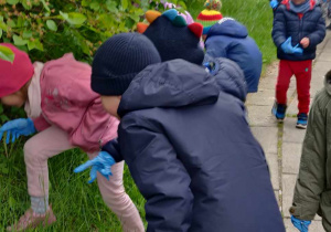 Dzieci w rękawiczkach zbierają śmieci z trawy.